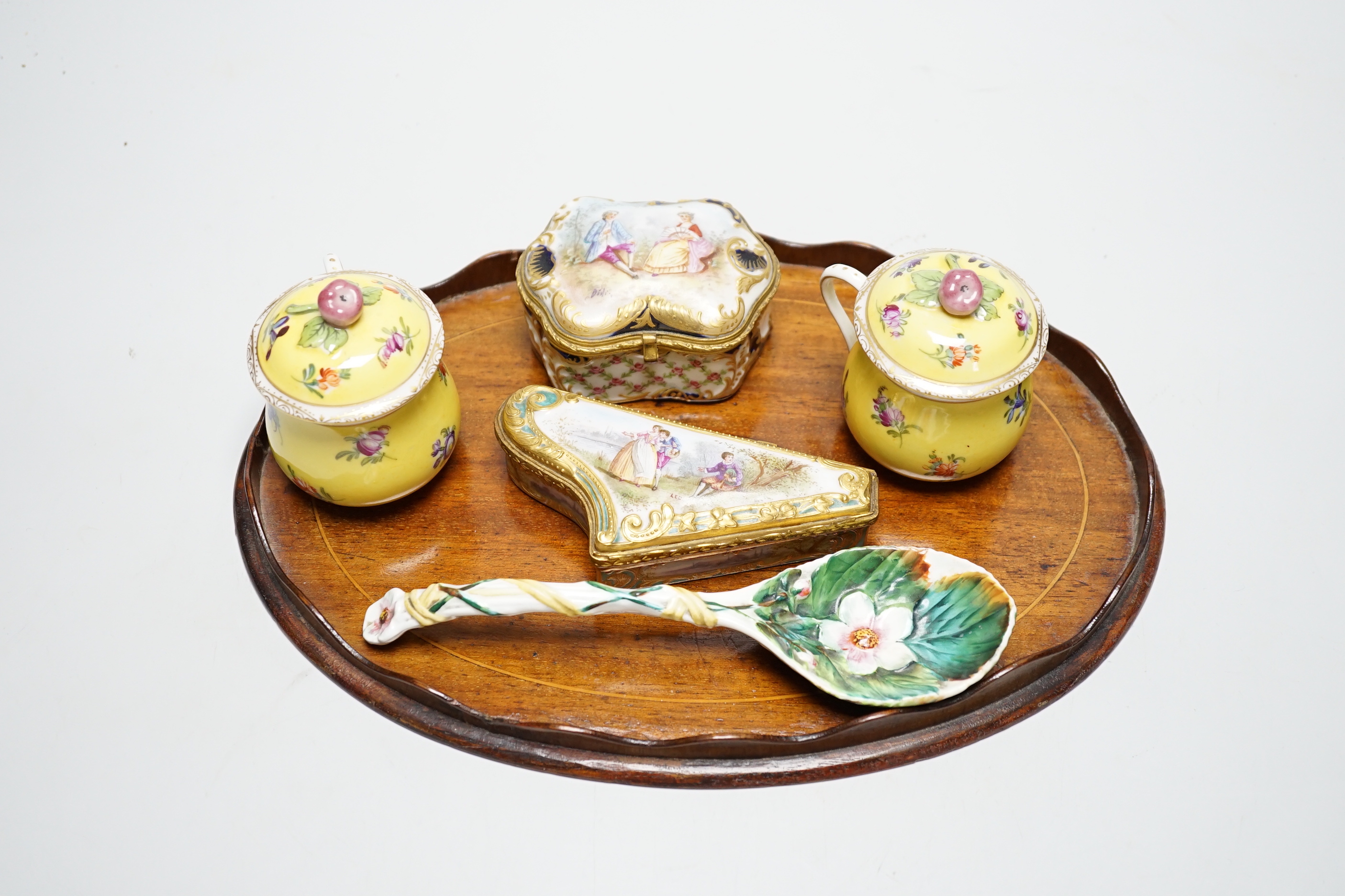 A small oval mahogany tray and German decorative porcelain cups and covers, two trinket boxes and a spoon